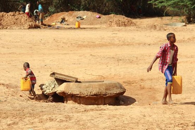 Zwei Kinder verlassen Brunnen mit Kanistern