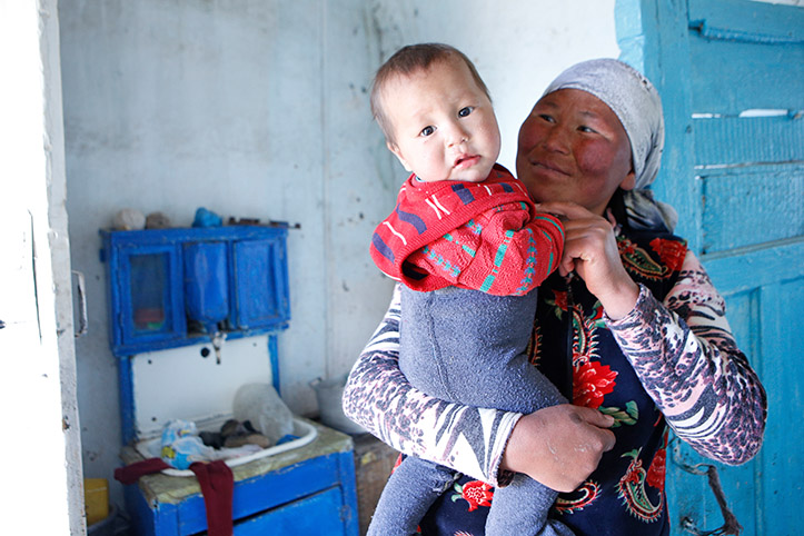 Kirgisin lächelt Kind in ihrem Arm an
